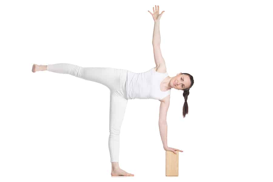 woman performing half-moon yoga pose with a yoga block demonstrating how to use yoga blocks for injury prevention. 