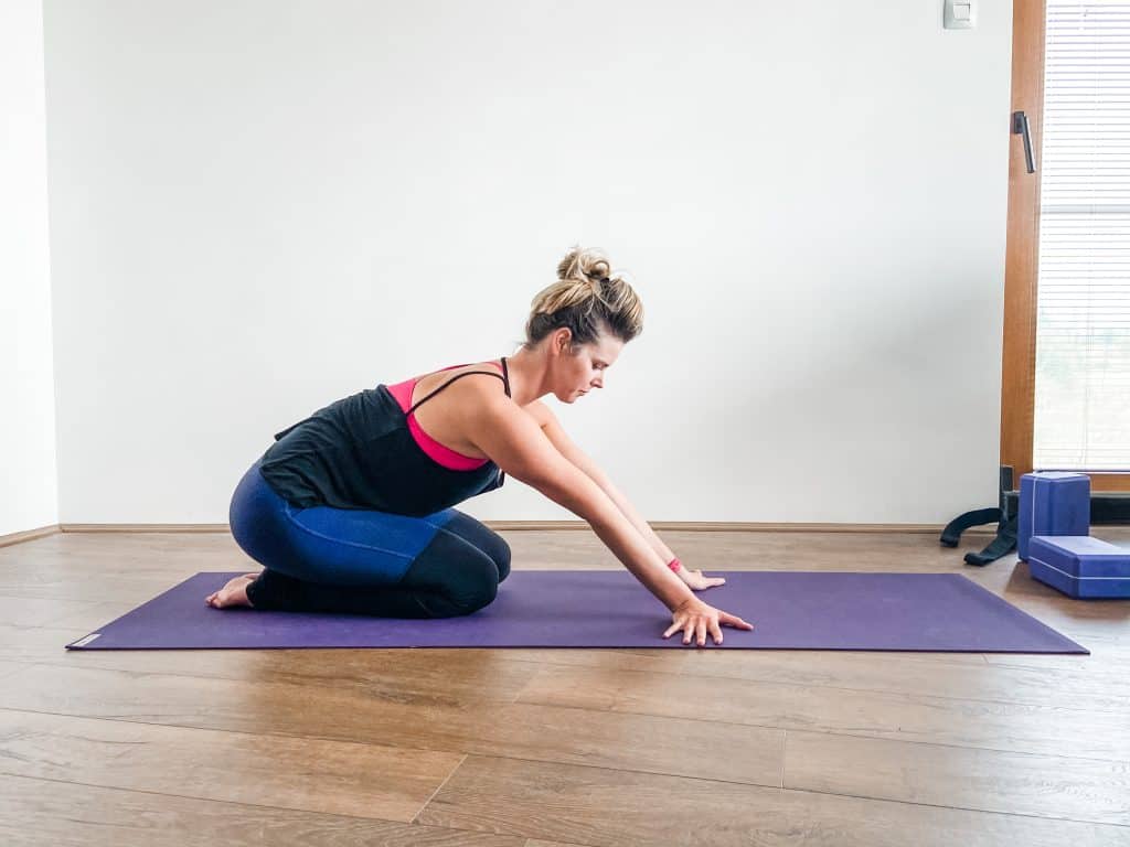 woman on a yoga mat demonstrating wrist stretching in kneeling position