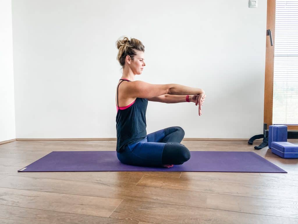 woman seated on a yoga mat demonstrating a wrist extensor stretch for elbow and wrist flexibility. 