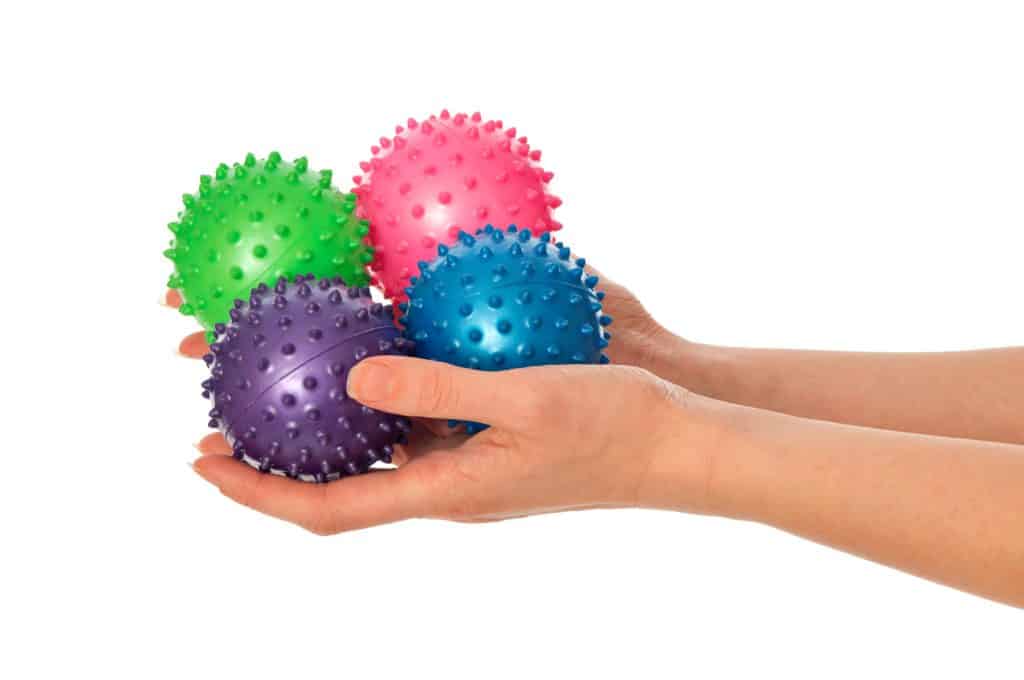woman holding different colored massage balls. decorative image for an article about physical therapy equipment for home. 